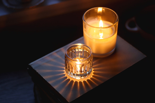 Vintage books, reading glasses, cup of tea or coffee, bowl of cookies, pumpkin and lit candles on the table. Hygge at home, fall atmosphere. Selective focus.