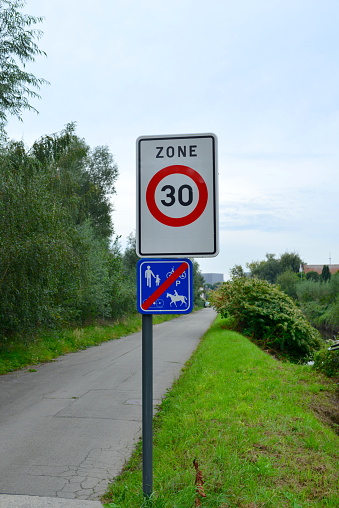 Close-up of a speed limit sign for 30 miles per hour on a narrow road through a British village.