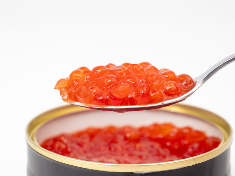 Open tin can with red caviar and a spoon on a white background. Red caviar close-up.