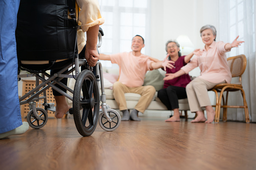 Close-up of senior woman in wheelchair with her caregiver in background and elderly friends are waiting to welcome