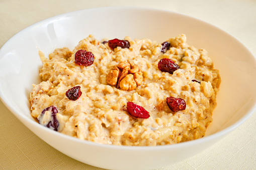 Tasty oatmeal porridge with walnuts and cranberries in bowl