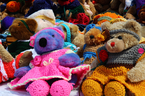A group of teddy bears of different colors and sizes wearing crocheted clothes. They look cuddly, adorable.The photo is heartwarming, nostalgic and evokes feelings of childhood innocence and comfort.