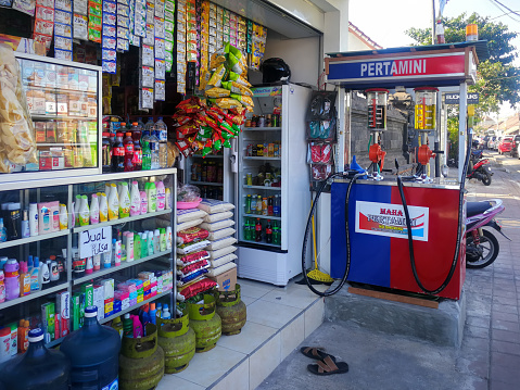 Gas station and pricing board of PTT station in Bangkok Ladprao. In background are buildings and street, at left side are several banners behind fuel pump