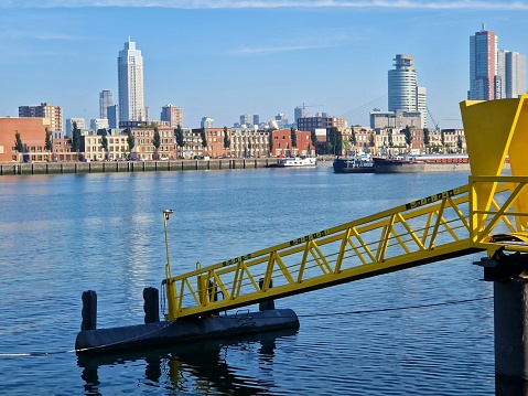 Industrial yellow mooring for water taxi in Rotterdam on the river Meuse with skyline in the background
