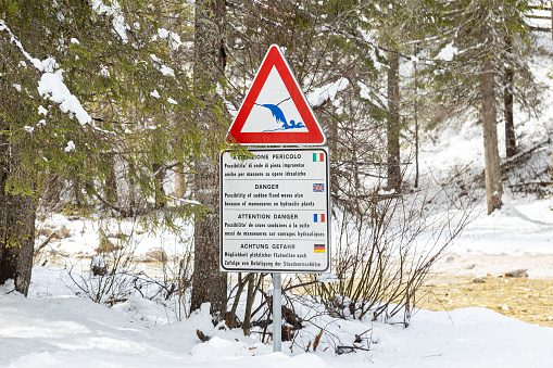 High water danger sign. Possibility of sudden flood waves after manoeuvres on hydraulic plants by Rienz river in a snowy winter day; Toblach (Dobbiaco), Bolzano, Italy; Dolomites