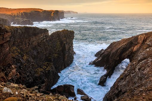 The rocky coastline of Dail Beag, near the famous Stac a' Phris sea arch,  on the Isle of Lewis, Scotland. The landscape is wild and untamed, with jagged rocks and cliffs that stretch out into the horizon.