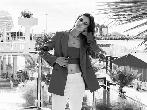 Black and white portrait of a beautiful brunette in a jacket, top and white trousers against the backdrop of the coastal sea