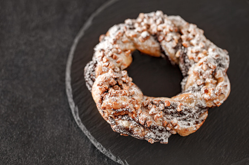 Brezel handcrafted sweet with nuts, on slate stone plate round, dark background, selective focus