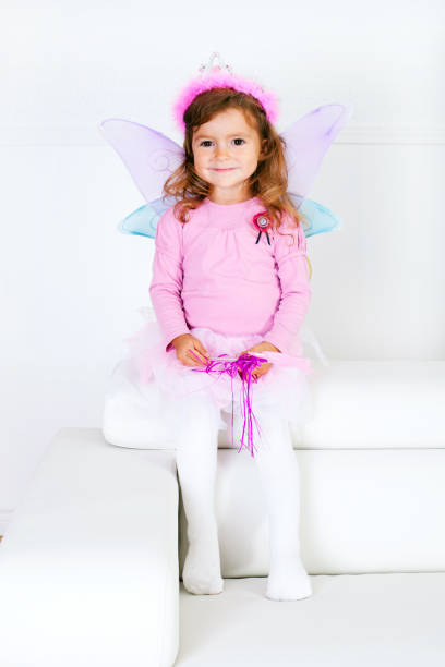 Cute girl wearing fairy costume holding magic wand jumping on bed.
