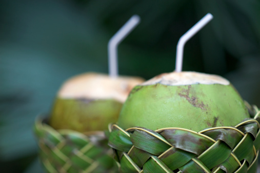 Fresh Brazilian coco gelado drinking coconuts in woven palm baskets rest on weathered wooden table against green jungle background