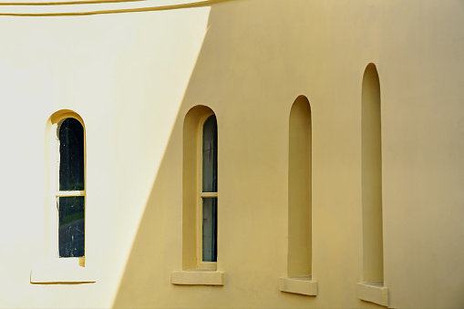 Narrow tall windows with arches on a yellow wall on a bright day