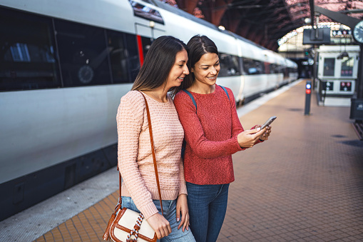 Two female friends at the train station looking at a mobile phone