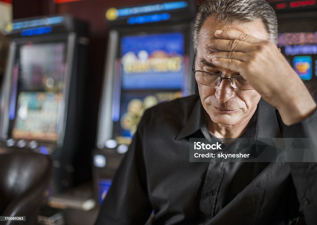 Uomo maturo compromettere il suo denaro su slot machine. - Foto stock royalty-free di Gioco d'azzardo