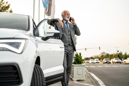 Senior business man talking on phone while entering in the car