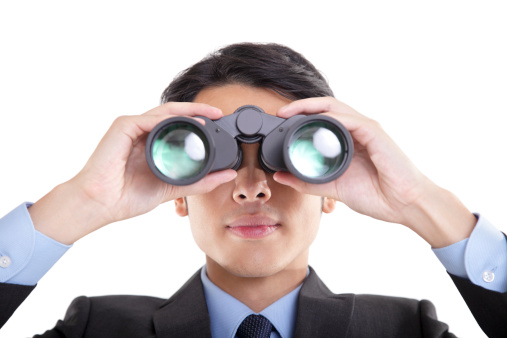 Front view of young Asian businessman looking through binoculars, isolated on white background.