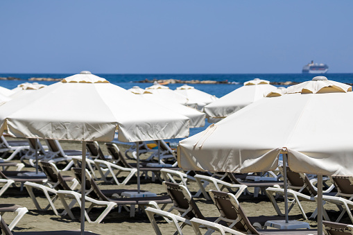 White canvas parasols and empty sunbeds on sandy sea beach, Limassol, Cyprus