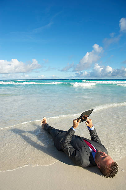 homme d'affaires se détend sur la plage à l'aide d'une tablette ordinateur - reading beach e reader men photos et images de collection