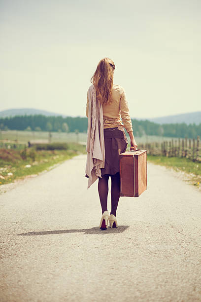 Woman walking on a country road with old suitcase