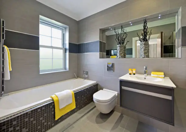 a lovely guest's bathroom in a luxury home taken with a wide angle lens to accentuate the angles whilst creating a strong composition. The colour scheme is shades of brown and grey tiles with white units (and matching pedestal) with dashes of bright yellow from the towels and toiletries. The vases in front of the mirror are made of porcelain.