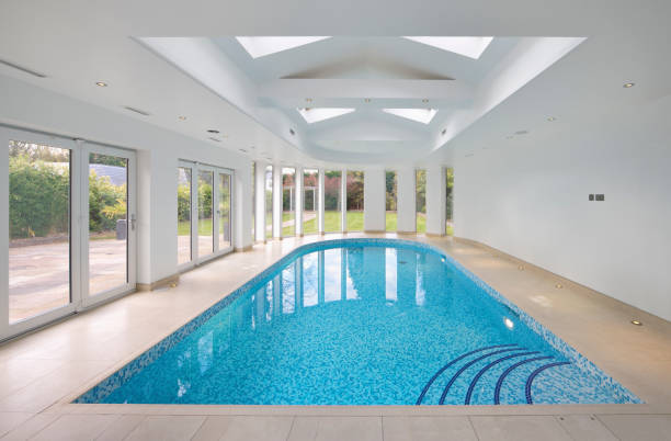 a lovely swimming pool in a luxurious new home taken during the day with view of the gardens through the patio doors. Mixed blue glass mosaic tiles line the pool whilst curved steps lead the viewer into the water... 