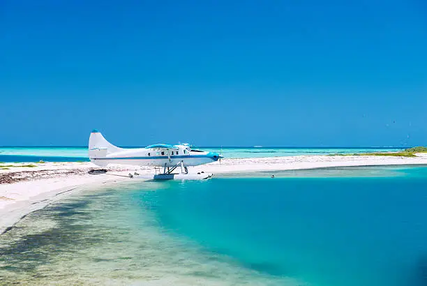 This is a horizontal, color photograph of a sea plane parked along the white sandy shores of Florida's Garden Key, an island in the Dry Tortugas National Park.