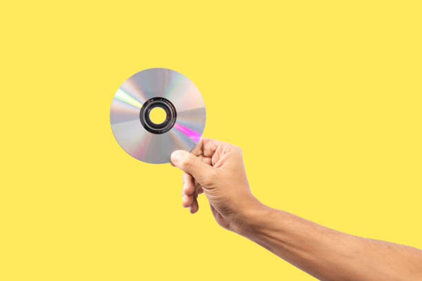 istock Black male hand holding a cd disc isolated on yellow background 1700946756