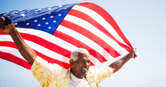 African American Senior carrying American flag on beach