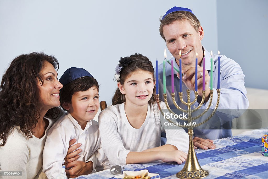 Jewish family celebrating Hanukkah Portrait of family celebrating Hanukkah, lighting Menorah.  Children aged 3 and 9 years. Hanukkah Stock Photo