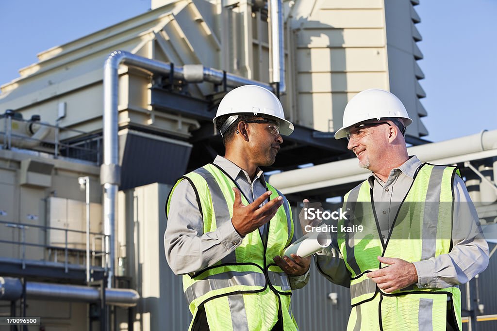 Engineers talking near power generator Multiracial male workers having discussion near power generator. (age 40s and 50s). Power Station Stock Photo