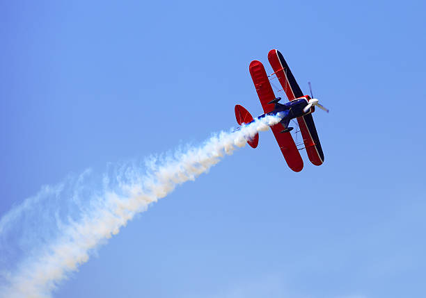 Aerial acrobatics stunt flying Aerial acrobatics - red propeller plane with smoke trail against clear blue sky aerobatics photos stock pictures, royalty-free photos & images