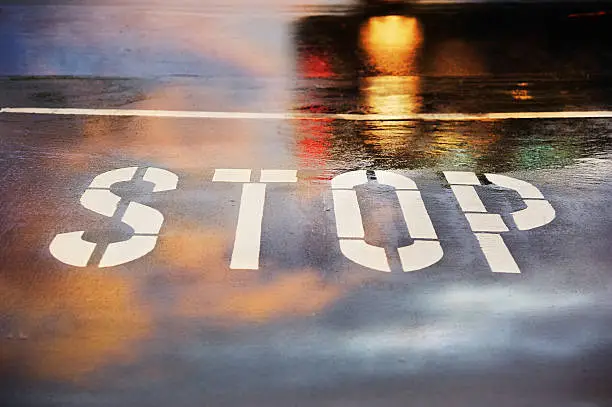Photo of Road junction, stop word, motion blurred car in pouring rain