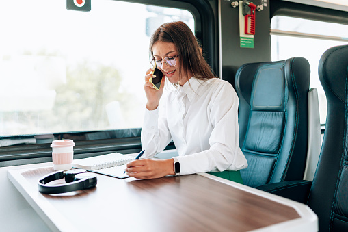 A young woman, seated cozily on the train, is engrossed in her mobile phone, finding ways to pass the time with digital entertainment