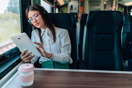 A young businesswoman is observed multitasking professionally with her digital tablet, making the most of her time on the train
