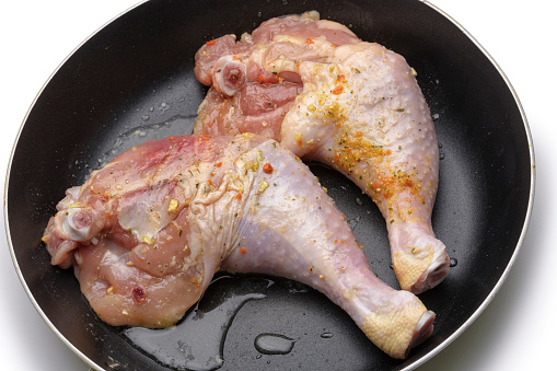 Two raw chicken drumsticks and legs in cooking pan with oil