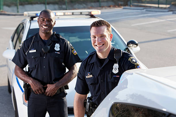 Police officers Multi-ethnic police officers (20s) standing in front of police car.  Focus on Caucasian man. police force stock pictures, royalty-free photos & images