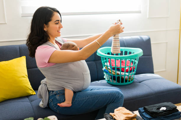 istock Beautiful mother using a baby carrier folding laundry 1700990990