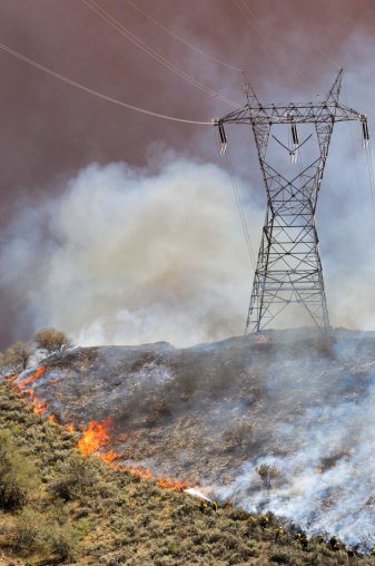 Small group of firefighters battling an out of control wildfire on a hillside, north of Los Angeles, with electrical pylon in background.