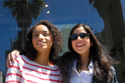 Two attractive young ethnic diverse women standing in front of store window, while shopping in Venice, Californa.