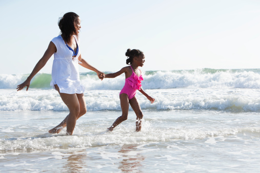 African American mother (30s) and daughter (6 years) at the beach, playing in the surf.
