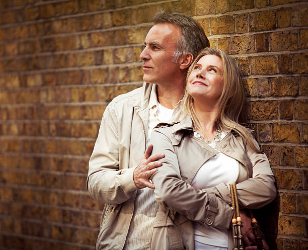 Smiling mature couple standing next to the brick wall.