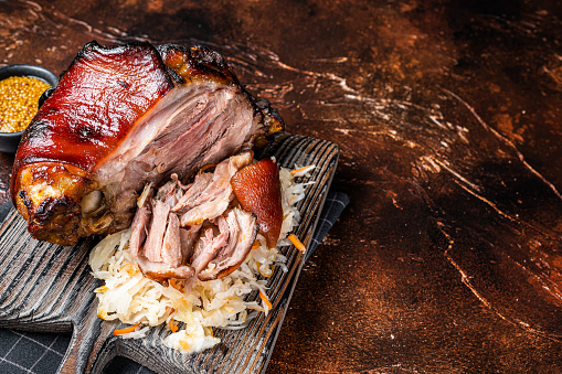 Schweinshaxe Roasted Pork Ham Hock, knuckle with Sauerkraut served on a wooden board. Dark background. Top view. Copy space.