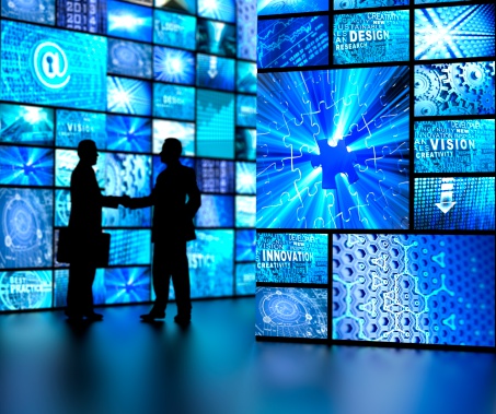 silhouettes of businessmen shaking hands and TV screens on wall showing business and technology related images 