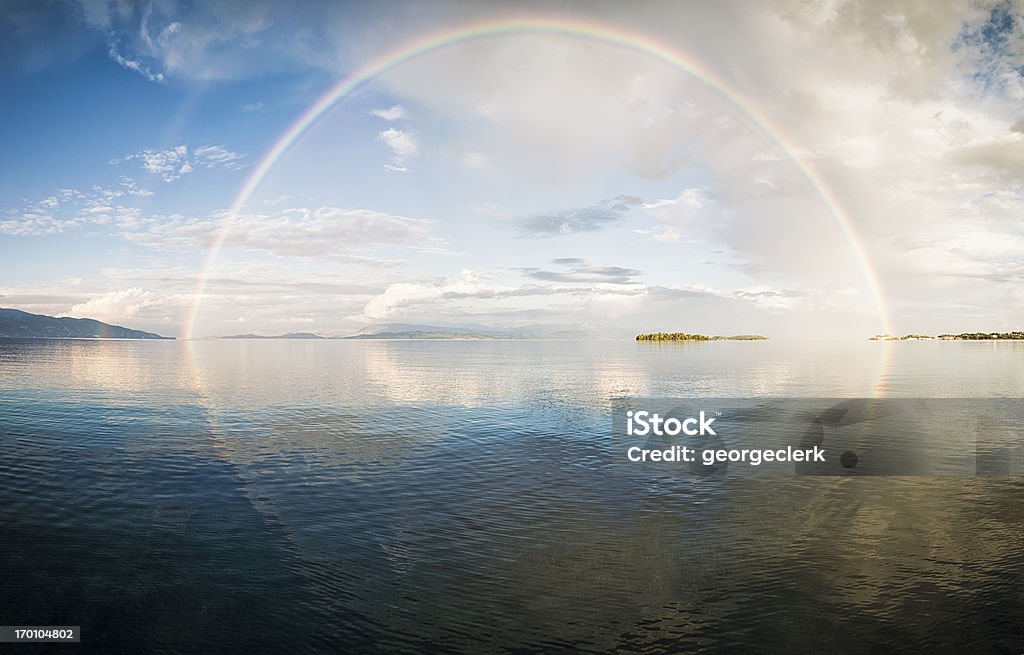 Full rainbow over the sea Panorama of a full rainbow reflected in calm water. Rainbow Stock Photo