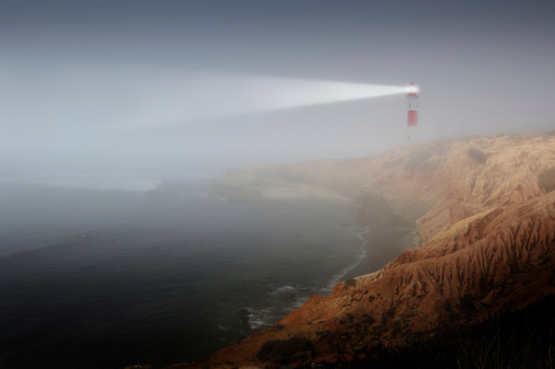 Red and white striped lighthouse beaming through deep fog.