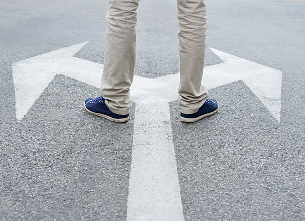 Man standing hesitating to make decision Man standing on arrows painted on asphalt. acute angle picture stock pictures, royalty-free photos & images