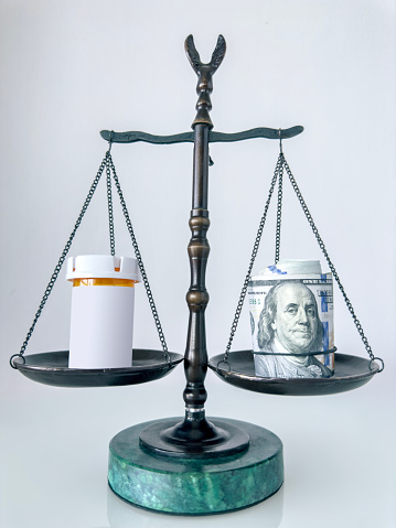 Still life of a scale of justice with roll of dollar bills and a pill box