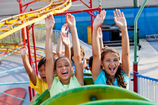 Multiracial children riding a roller coaster.  Focus on boy in yellow shirt.