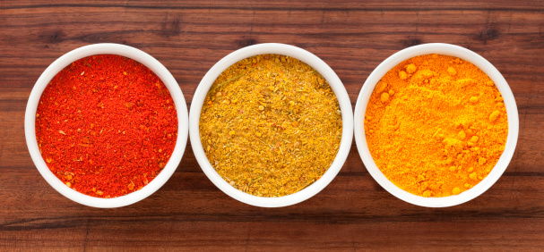 Three bowls containing ground spices (paprika, curry and turmeric)
