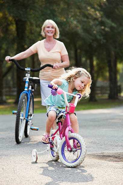petite fille avec sa grand-mère de vélo équitation - roue stabilisatrice photos et images de collection