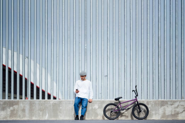 cycliste regardant son smartphone appuyé au mur - bmx flatland photos et images de collection